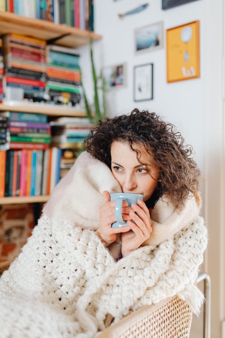 Woman wrapped in a chunky knit blanket, holding a blue mug of coffee